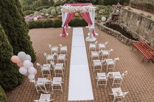 Boda decoración. muchos blanco sillas y un blanco camino. un blanco y rosado arco decorado con flores preparación para el Boda ceremonia. celebracion foto