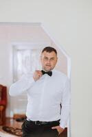 A stylish groom is tying his tie, preparing for the wedding ceremony. Groom's morning. A businessman wears a tie. The groom is getting ready in the morning before the wedding ceremony. photo