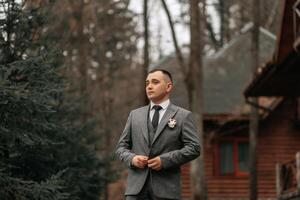 el novio en un gris traje poses durante un caminar en el bosque. negocio estilo. invierno boda. foto