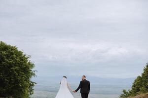 The bride and groom stand face to face with green hills in the background. A beautiful photo session of the bride and groom in the mountains. Free space.