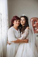 A beautiful and happy mother and her daughter, the bride, are standing next to each other. The best day for parents. Tender moments at the wedding. photo