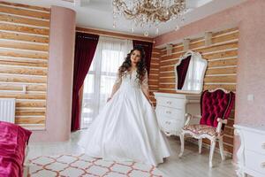 A wonderful beautiful portrait of a young bride. Beautiful bride with wedding makeup and jewelry wreath on long curly hair. Wedding photo model with brown eyes in a beautiful interior.