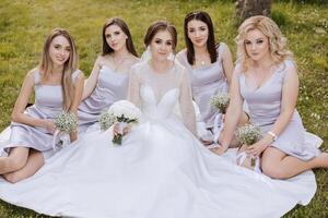 Group portrait of the bride and bridesmaids. A bride in a wedding dress and bridesmaids in silver dresses hold stylish bouquets on their wedding day. photo