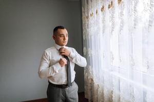 A man in a white shirt adjusts his tie. Business style. The groom on his wedding day photo