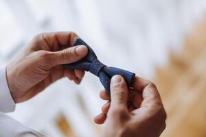 man's tie in hands, close-up photo of hands. The groom is preparing for the ceremony. Last preparations.