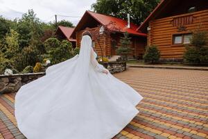 A red-haired bride is circling in her wedding dress, against the background of mountains and wooden houses. Magnificent dress with long sleeves, open bust. photo