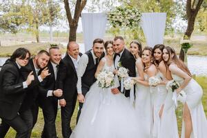 full-length portrait of the newlyweds and their friends at the wedding. The bride and groom with bridesmaids and friends of the groom are having fun and rejoicing at the wedding. photo