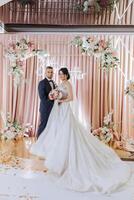 Wedding. Love and couple. Celebrating the ceremony and commitment. Save the date. Trust. The bride and groom embrace. Photo of a happy and bride and groom against the background of a ceremonial arch.