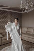 The bride is holding her exquisite wedding dress and posing in her room. Morning of the bride. Portrait photo