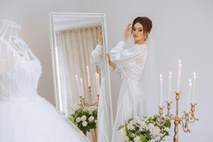 un hermosa morena novia es preparando para el Boda en un hermosa tocador estilo vestir entre Fresco flores y elegante candelabros en contra un espejo antecedentes. Boda retrato, foto. foto