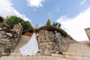 wide-angle photo of the bride and groom on the steps against the background of stone walls. Free space.