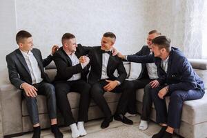 A young groom and his funny friends pose for the camera. A group of young people hug the groom and cheerfully congratulate him. Happy friends. Friends in the room. Wedding day. photo