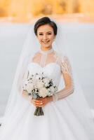 The bride holds a bouquet and poses during a walk in winter. Exquisite dress and hairstyle. photo