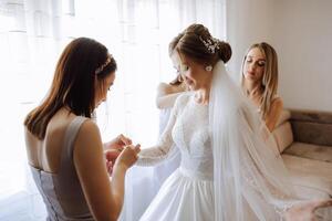 Morning of the bride. The bride's maid of honor helps the bride lace up her dress, fasten buttons on the dress or sleeves. Girlfriends help the bride fasten her dress photo