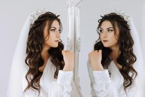 portrait of a luxurious bride in boudoir style near a mirror with reflection. Preparing the bride for the wedding in the morning in a white robe. photo