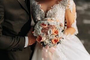 The bride is holding a beautiful wedding bouquet of pink flowers. White wedding dress with beaded sleeves photo