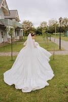 brunette bride in a lacy white dress with a long train, posing with a bouquet of white and pink flowers, against the background of trees. The veil is in the air. Beautiful hair and makeup. photo