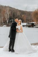 Wedding portrait. The bride in an elegant long dress, holding a bouquet, and the groom in a classic suit, stand hugging in the winter garden. photo