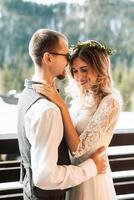 the groom embraces the bride against the background of snow-capped mountains. A wedding couple is celebrating a wedding in the mountains in winter. photo