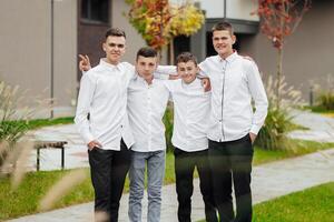 Group of smiling and happy teenage friends wearing casual clothes spending time together, posing and talking with each other near college building on autumn day. photo