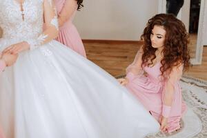 A friend helps the bride fasten her dress. A woman helps her friend fasten the buttons on the back of her wedding dress. The morning of the bride, the creation of a family, an important event. photo