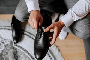 un elegante hombre usa negro cuero formal zapatos. atadura zapatos. negocio hombre atadura cordones de los zapatos en el piso. arriba cerca el novio es preparando para el boda. foto