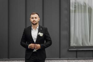 stylish and elegant groom in a black suit and white shirt on a dark background photo