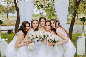 grupo retrato de el novia y damas de honor novia en un Boda vestir y damas de honor en blanco vestidos y participación elegante ramos de flores en el Boda día en contra el antecedentes de el lago. foto