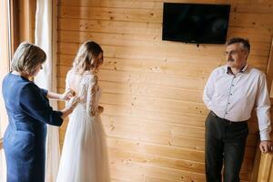 Photo with parents at the wedding. Happy parents help and rejoice for their soon-to-be-married daughter. Touching moments at the wedding. Mother ties the dress of her daughter's bride