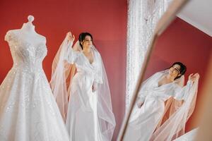 portrait of a luxurious bride in boudoir style near a mirror with reflection. Preparing the bride for the wedding in the morning in a white robe. photo