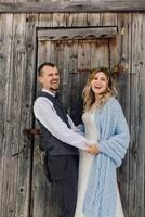 Groom and bride on the background of a wooden forest house. The bride is wrapped in a blue blanket. Winter wedding. photo