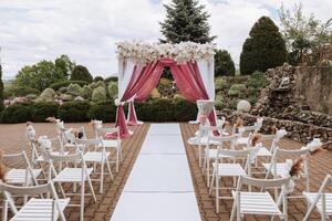 Boda decoración. muchos blanco sillas y un blanco camino. un blanco y rosado arco decorado con flores preparación para el Boda ceremonia. celebracion foto