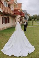 A beautiful young bride in a summer park is walking to her groom. Photo of the bride from behind. Beautiful wedding white dress. Walks in the park. A happy and loving couple.