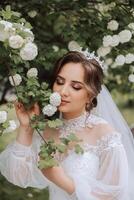 Rizado morena novia en un lozano velo y manga larga vestir poses siguiente a un blanco lila. hermosa pelo y constituir. primavera Boda foto