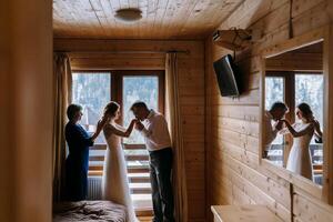 Happy parents help and rejoice for their soon-to-be-married daughter. Touching moments at the wedding. Mom ties her daughter's dress for the bride, dad tenderly kisses the bride's hands photo