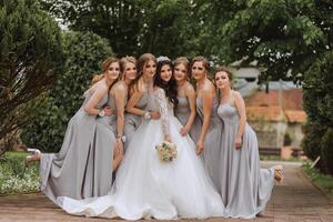 Group portrait of the bride and bridesmaids. A bride in a wedding dress and bridesmaids in silver dresses hold stylish bouquets on their wedding day. photo