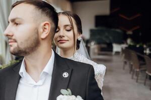 Lovely newlyweds. The bride hugs the groom from behind by the shoulders. Portrait of the bride and groom in a lace dress. photo