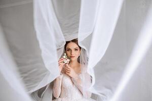 A luxurious bride with a beautiful hairstyle and a gorgeous dress is getting ready for the wedding ceremony in the morning. Morning photo of the bride at home or in a hotel room. Professional makeup.