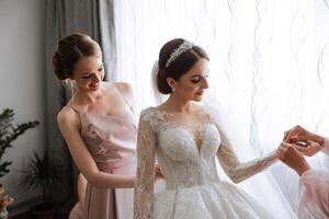 Morning of the bride. The bride's maid of honor helps the bride lace up her dress, fasten buttons on the dress or sleeves. Girlfriends help the bride fasten her dress photo