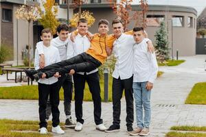 Group of smiling and happy teenage friends wearing casual clothes spending time together, posing and talking with each other near college building on autumn day. photo