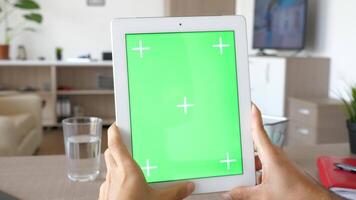 Digital tablet PC with green screen chroma mock up in male hands at a table over a video