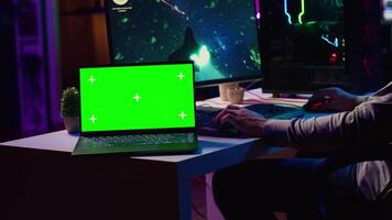 Green screen laptop next to man having fun by using gaming keyboard to fly spaceship in SF videogame. Mockup notebook and gamer using powerful PC and computer peripherals to play game video