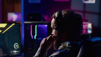 Man relaxing by playing futuristic science fiction videogame on PC at computer desk late at night. Gamer shooting enemies with lasers in online multiplayer first person shooter video