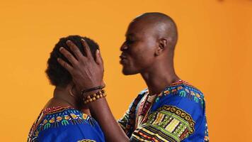 africano americano hombre besos su esposa frente en cámara y expresando sincero cierto sentimientos para su, dulce afecto. marido haciendo romántico gesto en estudio, cuidando acerca de su pareja. video