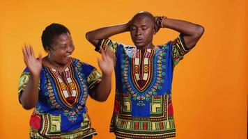 Joyful man and woman laughing together in studio, having fun with silly jokes over orange background. African american people enjoying funny moments with laugh, amused couple. video