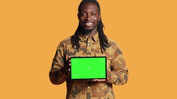 Male model holding laptop with greenscreen layout in studio, posing with isolated display copyspace on pc. Young adult presenting computer with blank mockup template on camera. video