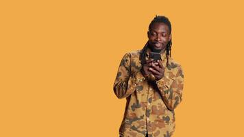 African american guy navigating on social media app, using smartphone to check online websites in studio. Male model browsing internet pages on phone network, smiling on camera. video