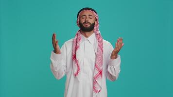 Islamic guy turns to Allah for hope trusting in sacred meditation over blue background. Middle eastern person honoring God through holy ritual, showing devotion and praying. video