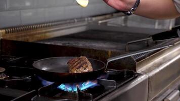 Pouring souce on piece of grilled fryed beef meat in restaurant kitchen then cooking it with open flame video