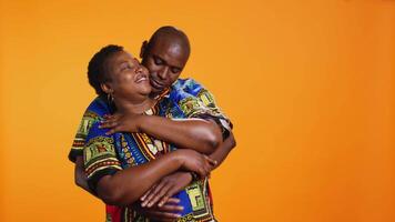 Sweet african american couple embracing in studio, holding each other and expressing their sincere feelings. Ethnic romantic man hugging his wife on camera over orange background. video